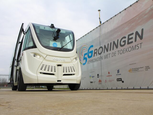 Zelfrijdende elektrische witte shuttlebus van het Franse bedrijf NAVYA geparkeerd naast een banner van 5Groningen: verbonden met de toekomst.