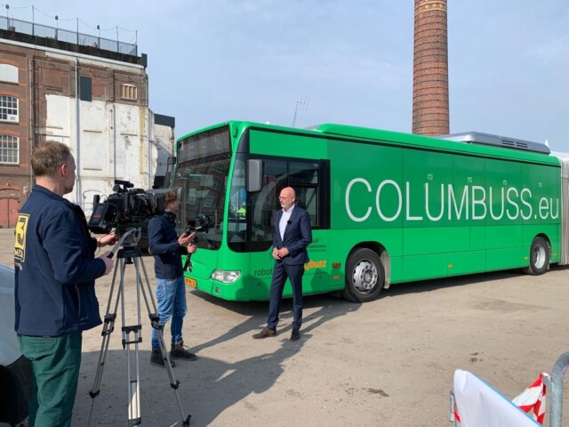Michel van der Mark van Qbuzz wordt gefilmd, op de achtergrond staat een groene bus.