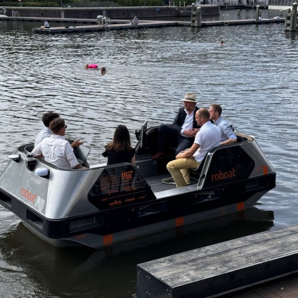 Een groep van zes mensen zit in een klein vaartuig genaamd "roboat".