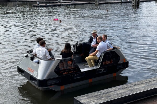 Een groep van zes mensen zit in een klein vaartuig genaamd "Roboat".